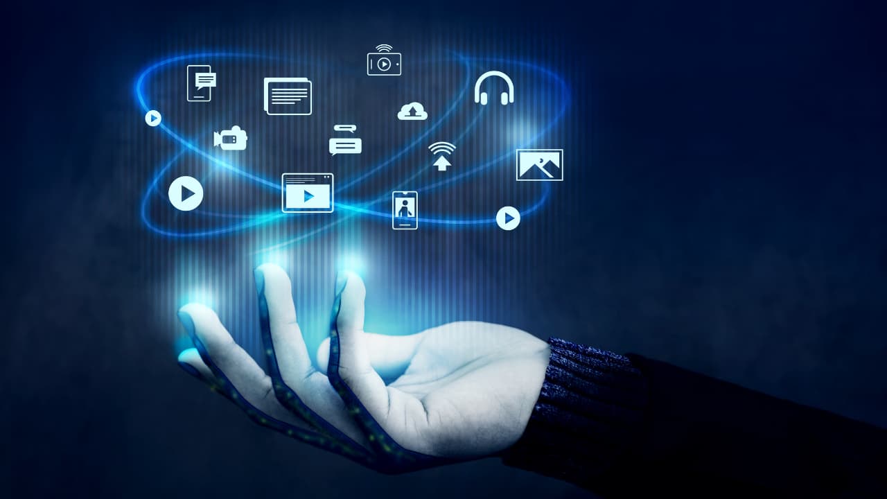 A hand is shown against a dark blue background, with glowing icons representing media, communication, and technology floating above it.