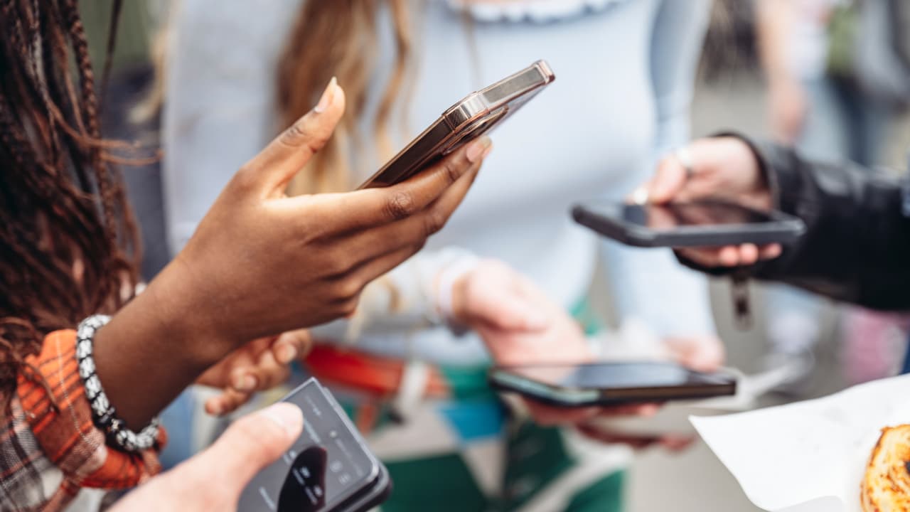 Close-up of diverse hands holding smartphones, engaging with screens. The atmosphere is social and connected, highlighting digital interaction among friends.