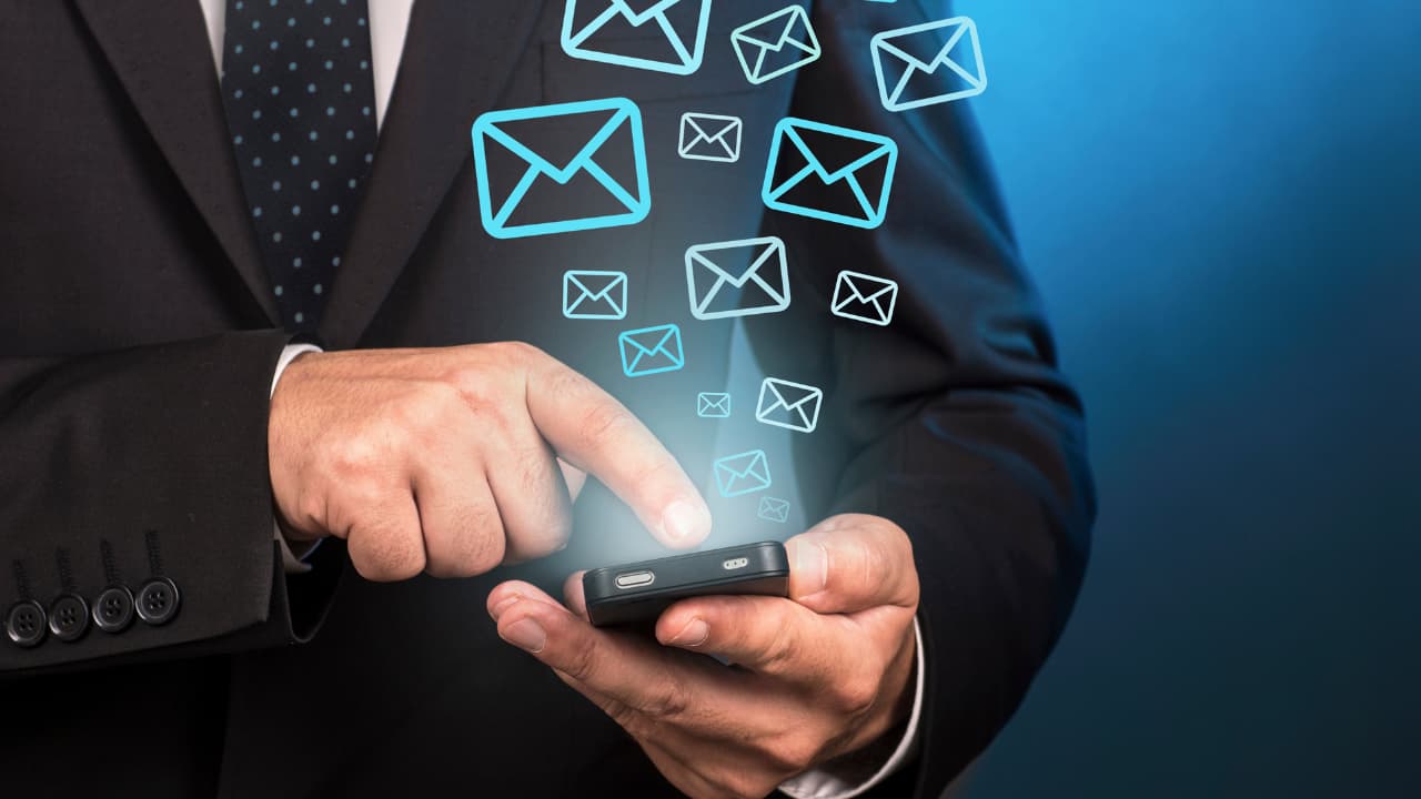 A person in a suit uses a smartphone, emitting glowing email icons. The scene conveys a sense of communication and connectivity.