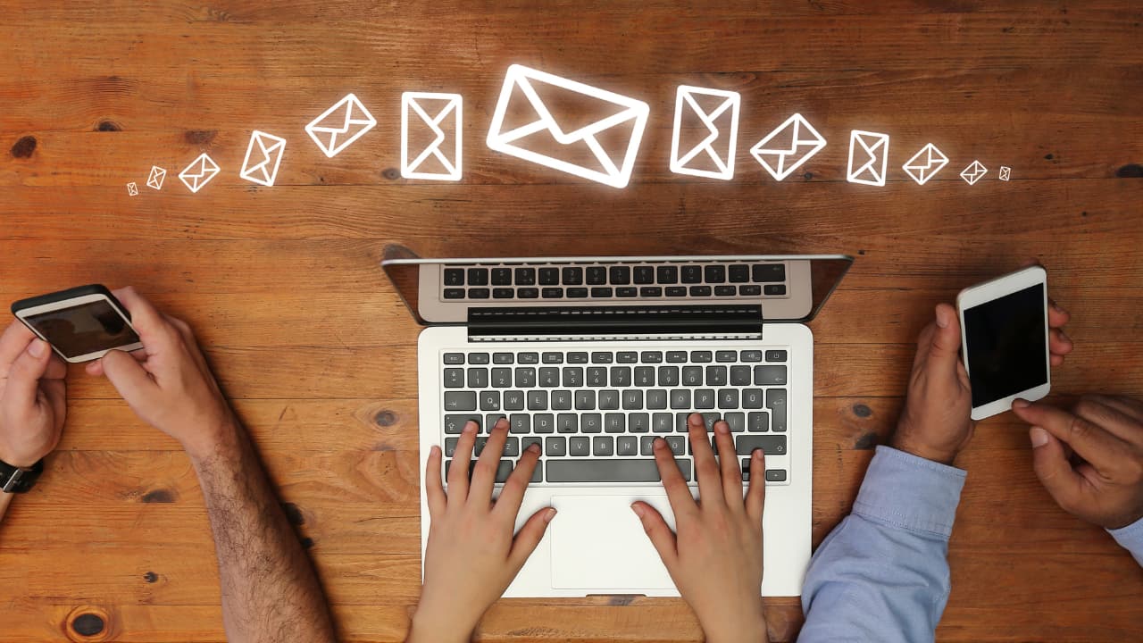 Two hands type on a laptop, flanked by hands holding phones. Floating email icons suggest communication and connection in a tech setting.