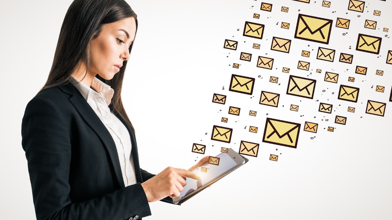 A woman in a black blazer uses a tablet, with numerous email icons floating from the screen. The image conveys digital communication and connectivity.