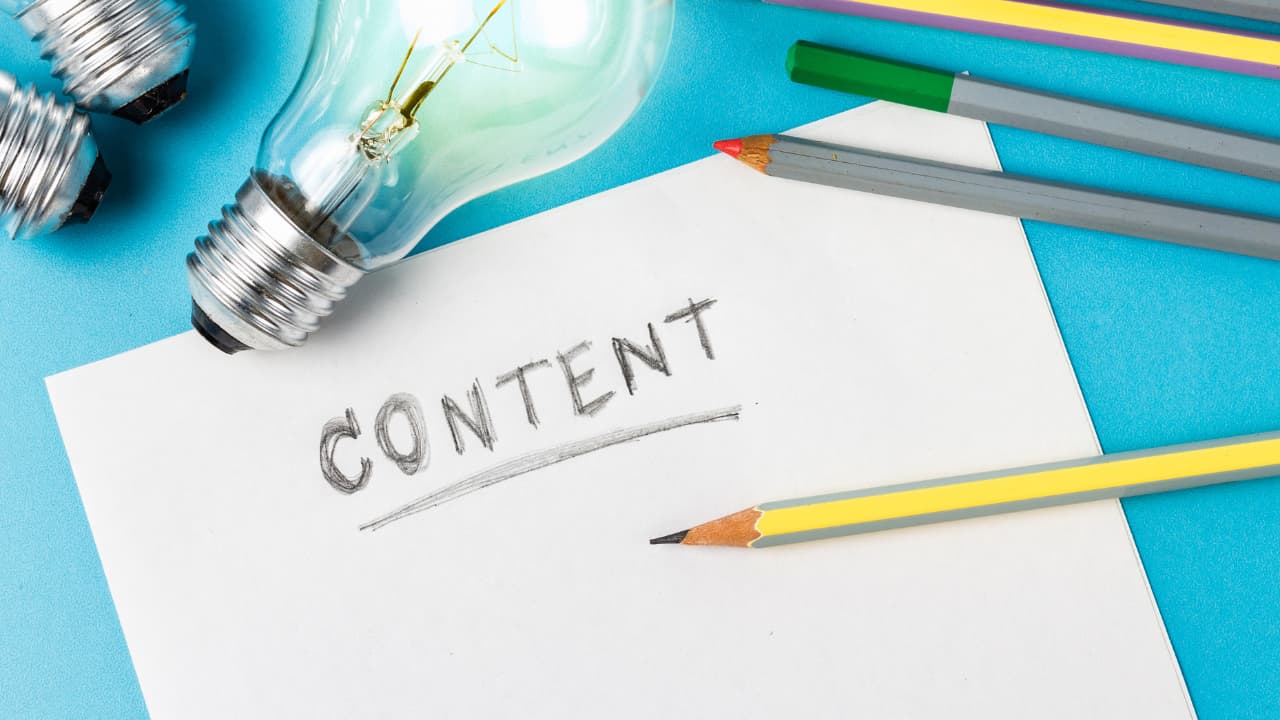 A light bulb and pencils surround a paper with "CONTENT" written on it, suggesting creativity and ideas. The background is a bright blue.