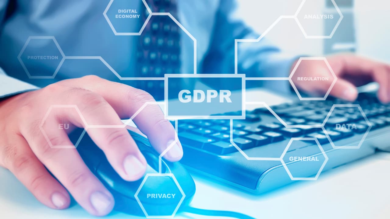 A close-up of hands using a computer mouse and keyboard, overlaid with hexagonal graphics featuring words like GDPR, Privacy, and Data. The tone is technological and professional.