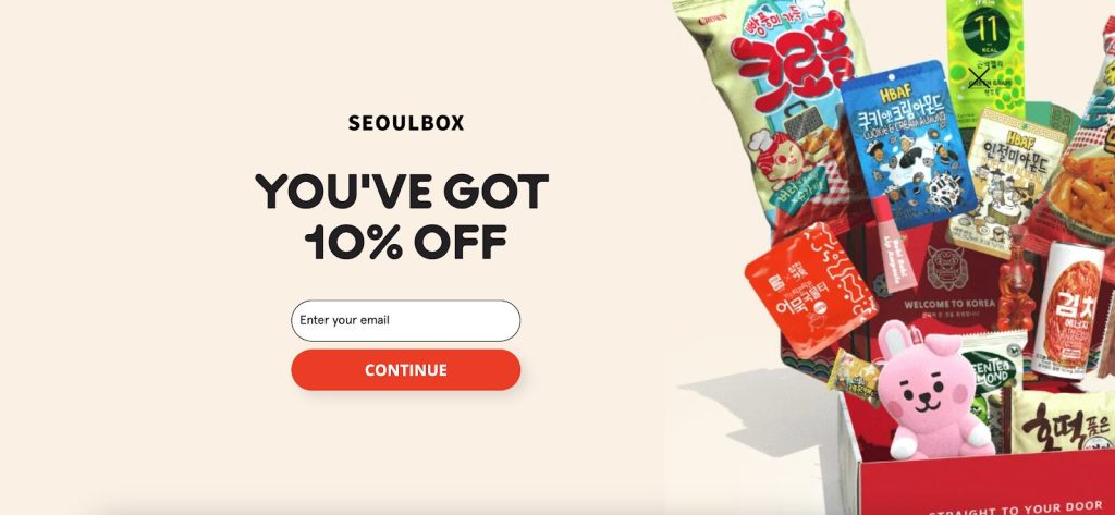 SeoulBox promotion offering 10% off. Korean snacks, K-pop, or K-beauty. Right features a box filled with Korean snacks, colorful wrappers, and a pink bunny toy.