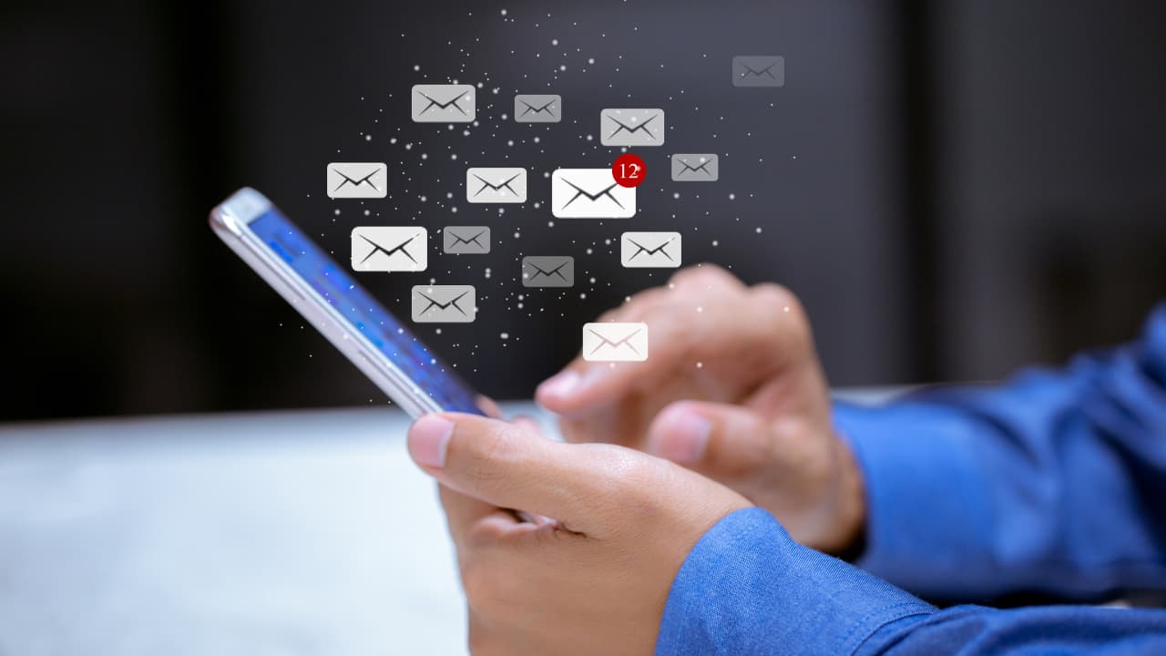 A person in a blue shirt holds a smartphone, with digital envelopes floating above, one showing 12 unread messages, conveying busyness and connectivity.