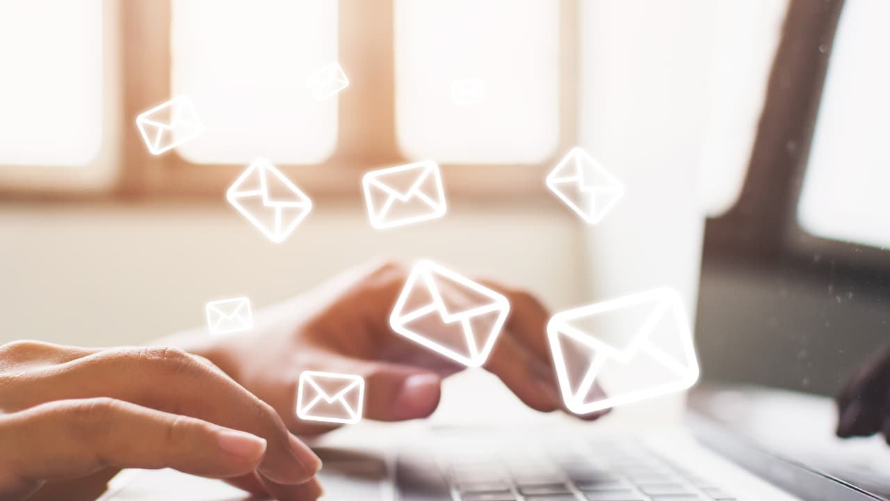 Hands typing on a laptop keyboard with bright, semi-transparent email icons floating above, suggesting digital communication and connectivity.