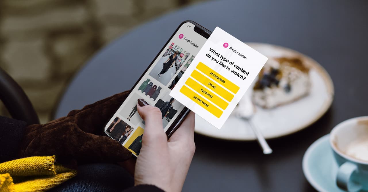 A person holding a smartphone displaying a fashion app, with content category options like accessories and shoes. Coffee and cake on a table create a cozy setting.